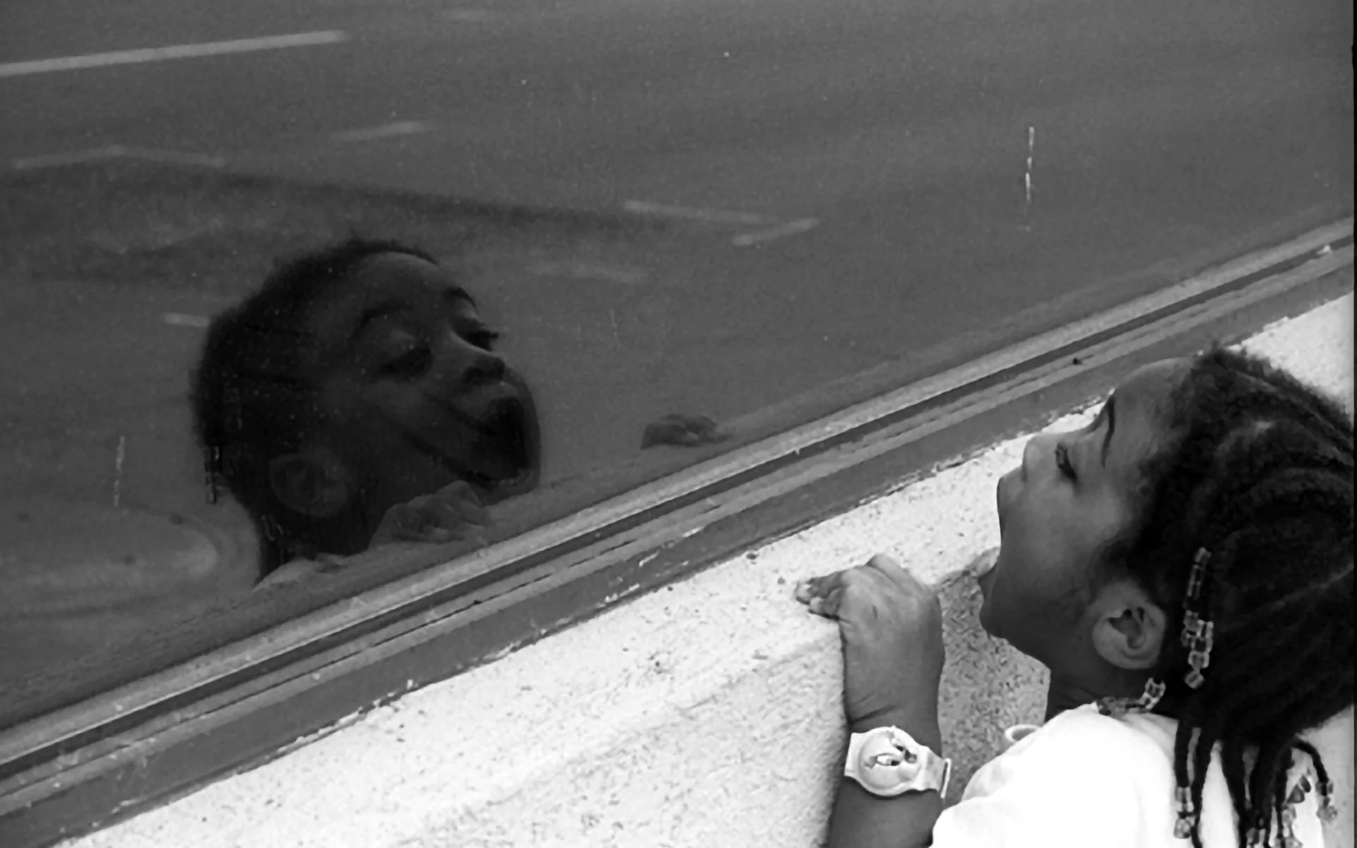 A child looking toward her reflected face in a building window.