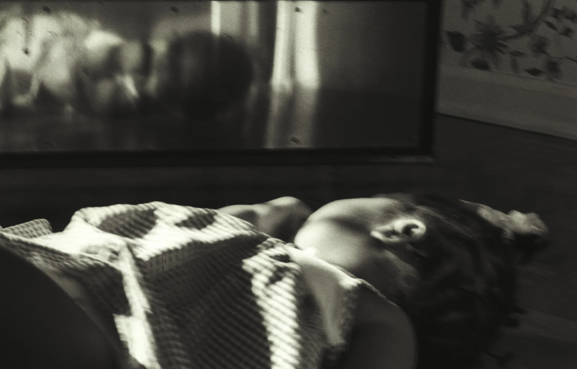 A child lying near a kick plate at the bottom of a door, her face reflected in the metal.
