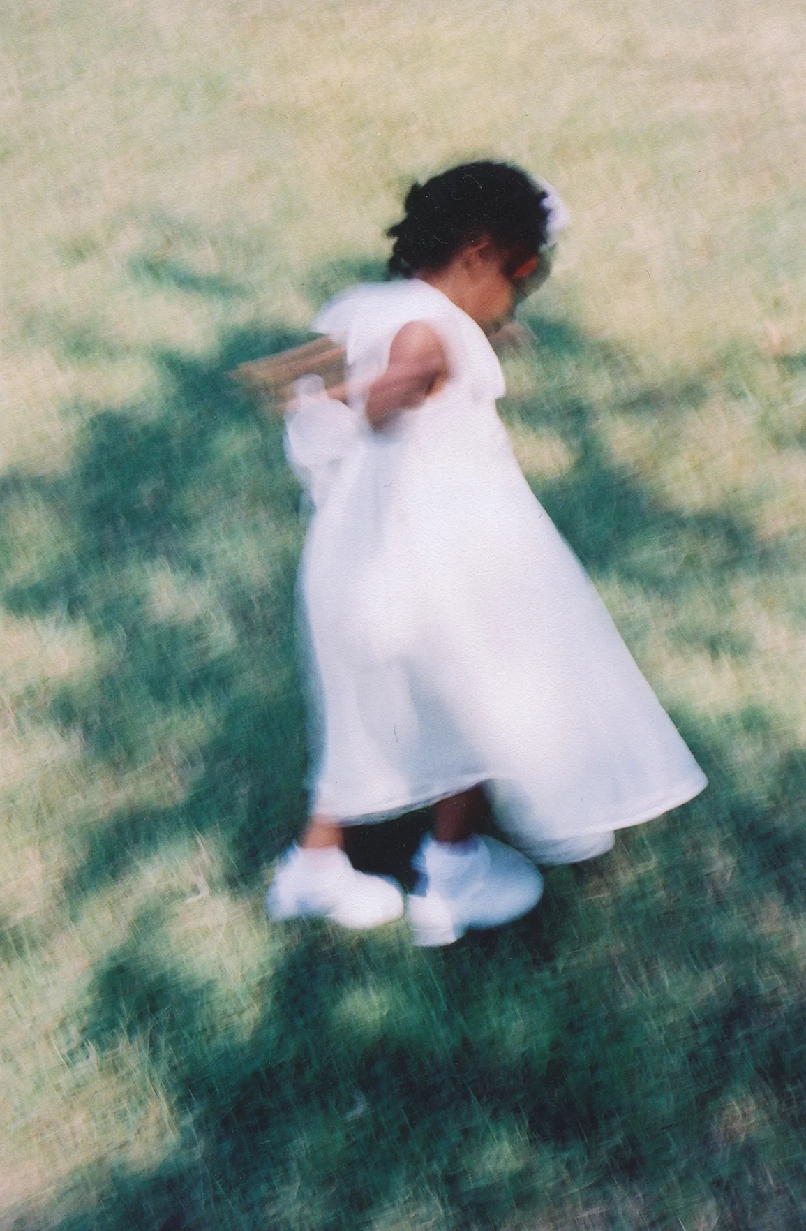 A child in a white dress moving through a sunlit lawn, rendered with intentional motion softness.