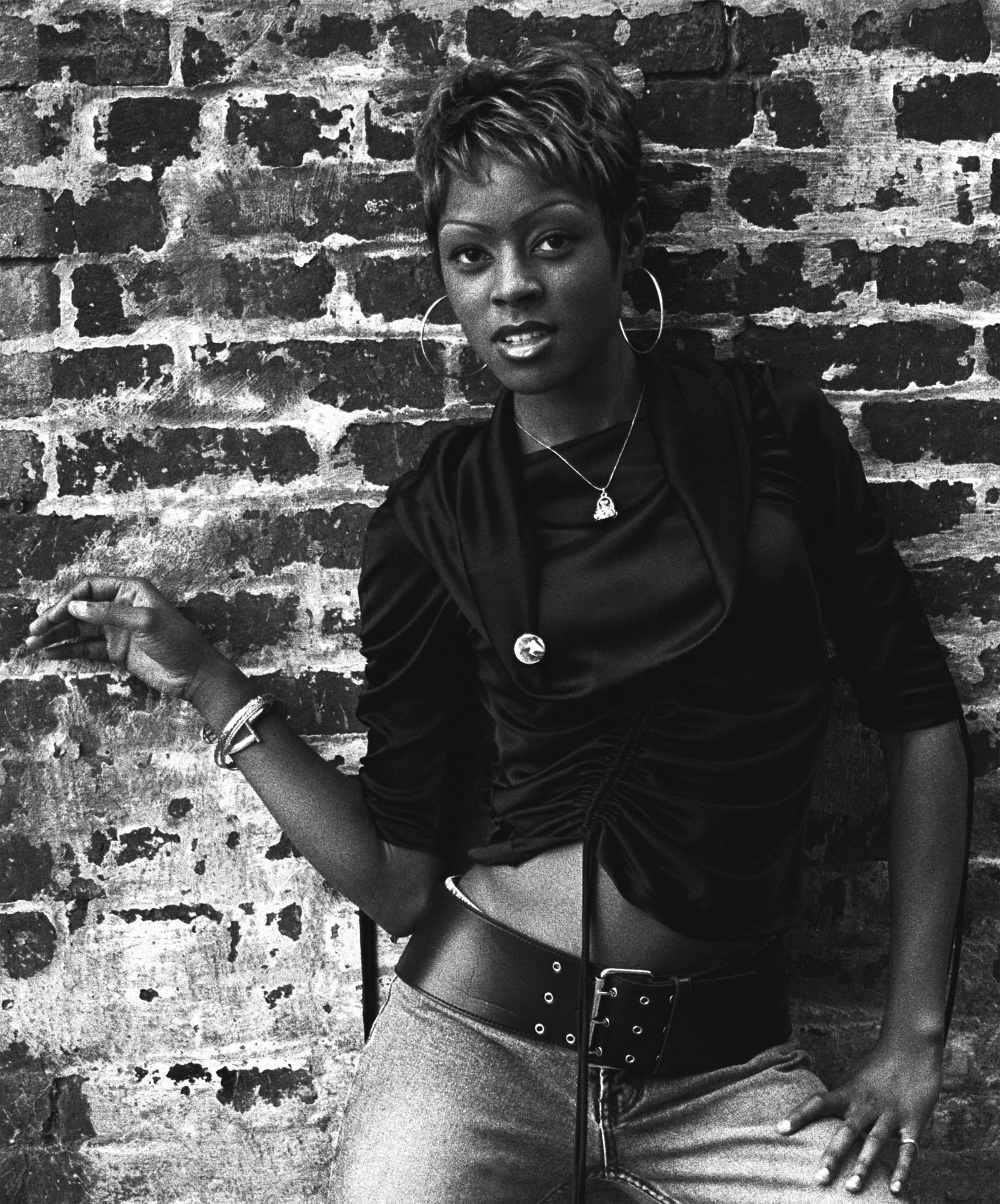 Black-and-white environmental portrait of a woman posed against a brick wall.